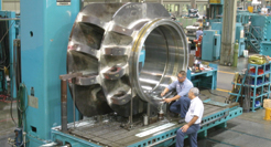 Two men soddering on a giant silver gear in Dril-Quip's Houston Facility
