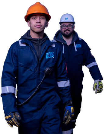 Two Dril-Quip workers wearing coveralls, hardhats, and work gloves, walking forward.