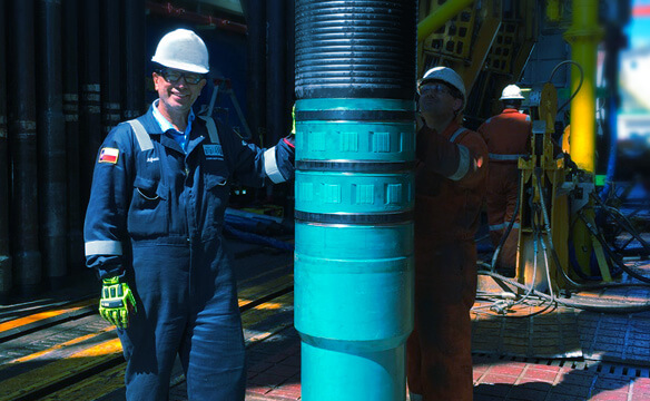 A smiling Dril-Quip employee standing next to a liner hanger at an active drill site.