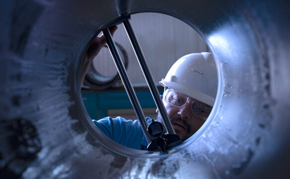 A Dril-Quip employee looking down a pipe while applying clamps
